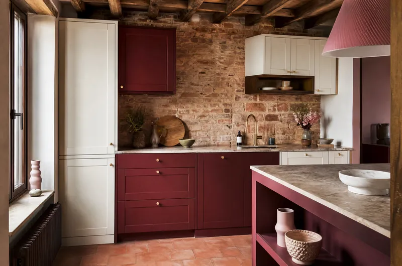 Cuisine rénovée dans une maison ancienne : mur de briques, poutres et meubles ajustés aux murs irréguliers